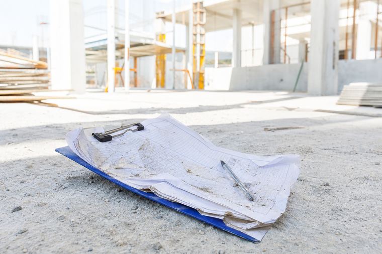 Uomo in giacca e cravatta in piedi vicino a un pilastro grigio, in una giornata di sole.